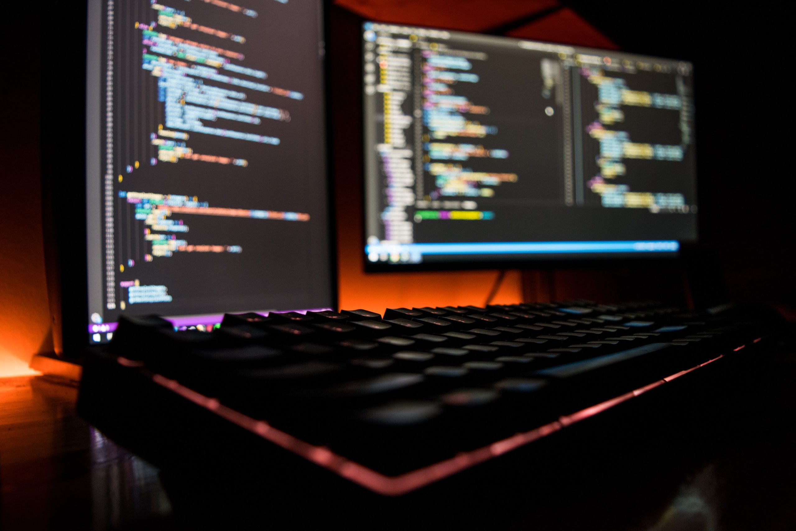 rgb keyboard with blurred pc monitor using vscode in the background