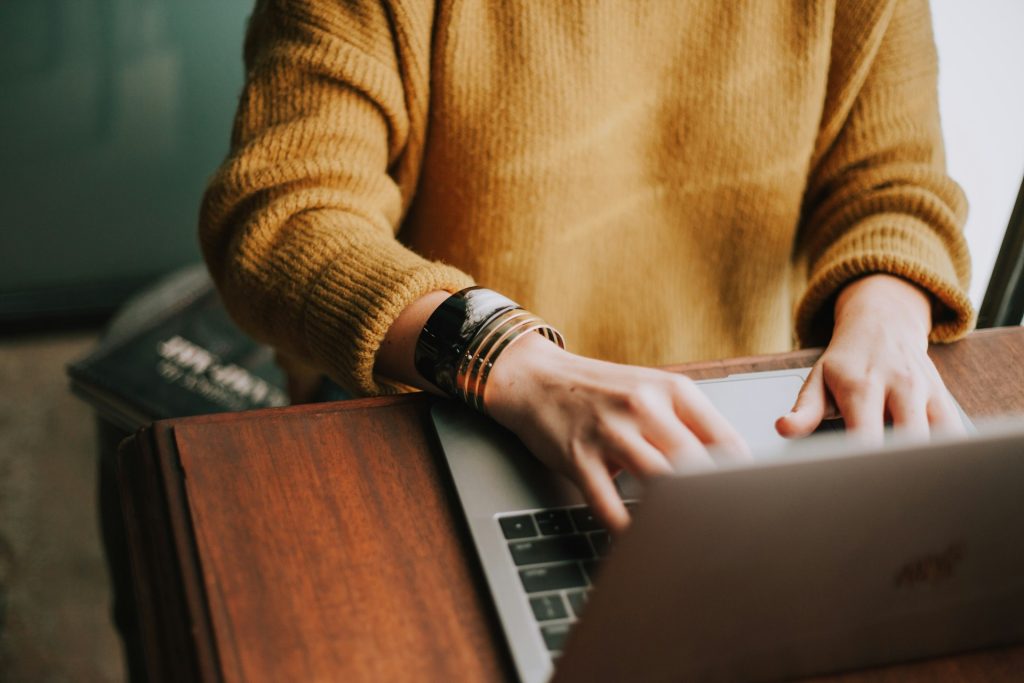 a woman in a mustard sweater using a laptop